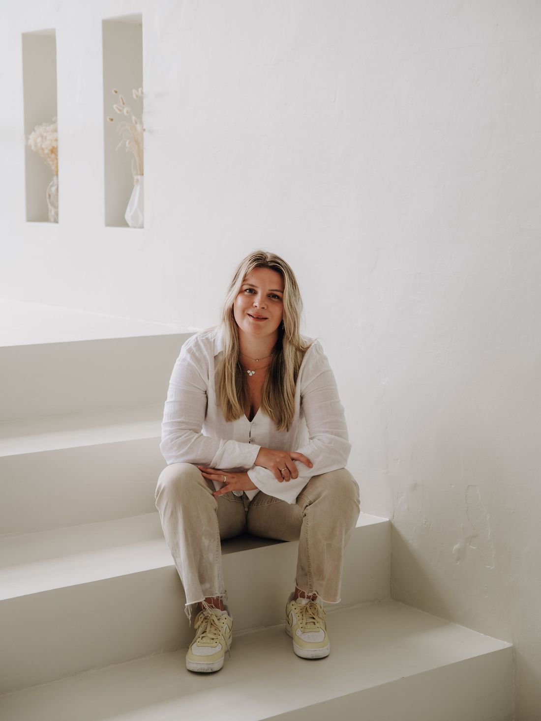 Anna Beils, systemische Coachin aus Lohmar, sitzt lächelnd auf einer hellen Treppe