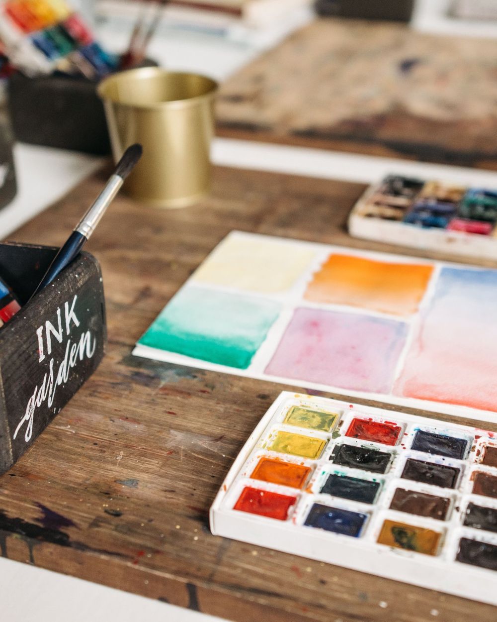 Aquarellfarben, Pinsel und Farbverläufe auf einem Holztisch – Material für den Kreativ-Workshop